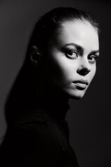 Intense portrait of a young woman with long dark hair, showcasing dramatic lighting and shadows, highlighting her strong facial features and thoughtful expression.