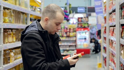 Focused male shopper examining red product bottle label, comparing ingredients and evaluating...