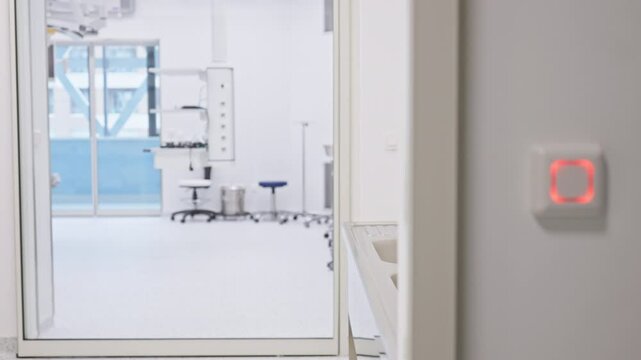 Hand interacts with an illuminated touch sensor on a white wall, controlling access to a modern medical facility with sterile, bright interiors. Concept of secure medical access systems