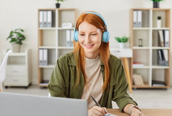 Portrait of a young redhead woman student sitting at the desk on workplace in casual clothes and...