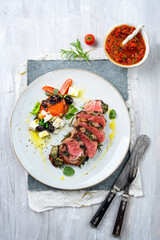 Traditional Italian Tagliata di Manzo beefsteak medailons with tomato relish, feta cheese and olives served as top view on a classic design plate