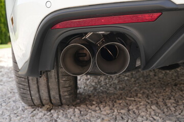 Na zdjęciu widoczny jest tył samochodu, a dokładniej fragment zderzaka wraz z podw&oacute;jną końc&oacute;wką układu wydechowego. Auto stoi na podłożu z jasnych kamyk&oacute;w, a obok widać tylną oponę pojazdu.