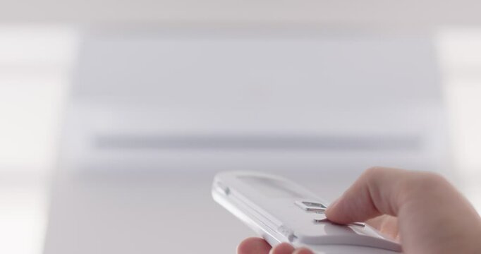 Operating remote controller in hand using air conditioner close up, switch, setting temperature in room, to feel comfortable indoors, domestic appliance proper cooling or heating, ventilation system