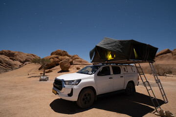 Camping. The SUV is parked in the Namibian desert, surrounded by beautiful boulders and stars. © Agil