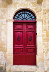 Traditional arched red door with large doorknobs in Mdina, Malta