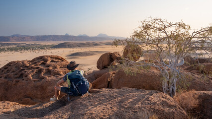A tourist sits on a hill and admires the landscape of the Namibian desert