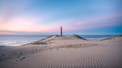 A peaceful scene of a lighthouse atop coastal sand dunes, with rippled sandy textures and pastel sunset skies blending into the tranquil ocean horizon.
