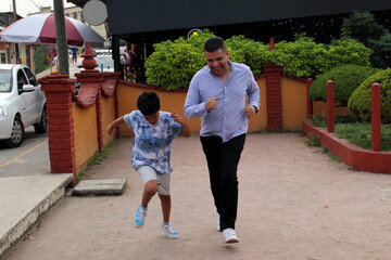 Latino dad and dark-skinned 9-year-old son play a speed race in the street, they have fun and are happy in poverty