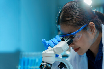 Scientist wearing gloves and protective glasses using microscope, conducting research in laboratory...