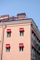classic-style historic pink house with red awnings on windows. sunny day. stylish architecture in center of metropolis. hotel or apartment building
