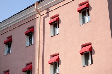 classic-style historic pink house with red awnings on windows. sunny day. stylish architecture in center of metropolis. hotel or apartment building