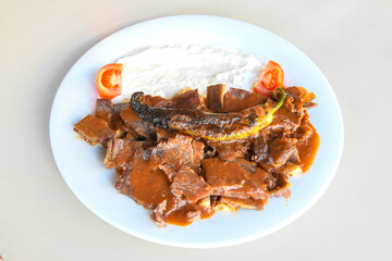 Turkish  Traditional Ramadan doner kebab with tasty tomato sauce and rice or turkish pilav in white plate on table background. Lavash doner kebab ( doner zurna durum )  Pilavustu doner Iskender kebap