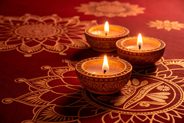 Hyperrealistic, cinematic close-up of three glowing diyas on a dark red background with gold intricate patterns. Golden hour lighting, - generated by ai