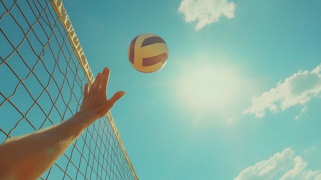 A volleyball player's hand reaches for the ball against a bright sunny sky. The net is visible in the foreground.  A perfect summer sports image.