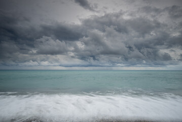 Dark clouds gathering over a turquoise ocean with soft waves crashing on shore