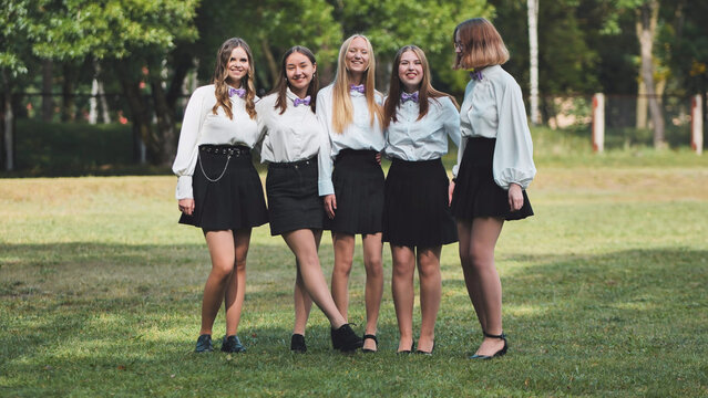 Five high school students in white shirts and bow ties happily reunite for their first day back at school in a park