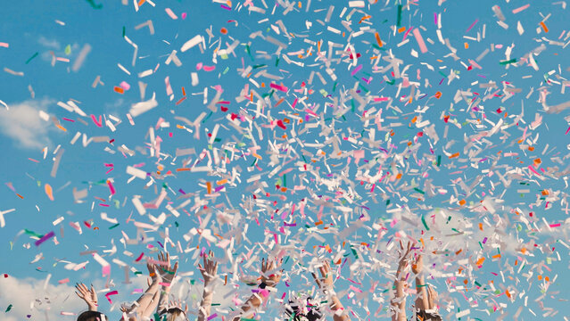 High school graduates joyfully tossing vibrant confetti in the air against a sunny blue sky