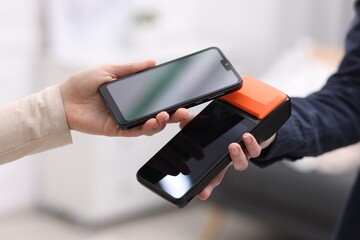 Woman paying with smartphone via terminal against blurred background, closeup
