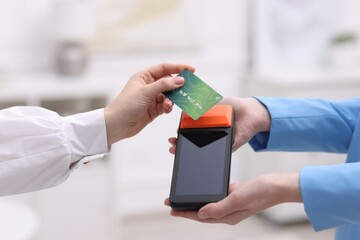 Woman paying with credit card via terminal against blurred background, closeup