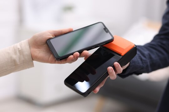 Woman paying with smartphone via terminal against blurred background, closeup