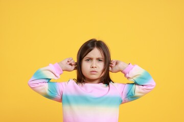 Annoyed little girl covering her ears from loud sound on yellow background