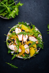 Salad with chicken fillet, juicy orange, sweet raisins, walnut, arugula, spinach and useful seeds, black background, top view