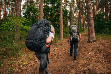 A happy married couple in love on a hike with a child in a backpack carrying a backpack goes up the mountain and overcomes a difficult path together