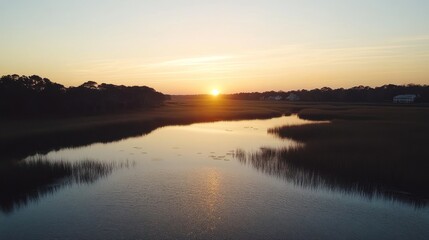 Fototapeta premium Serene sunset over calm river reflecting golden light, tranquil marsh landscape.