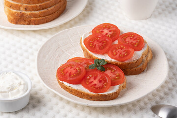 Delicious open-faced sandwiches topped with fresh tomatoes and cream cheese served on a textured white plate