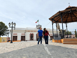 Dark-skinned Latino man and woman couple walk along the cobblestone streets of a magical town as...