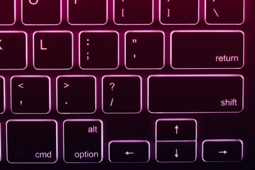 Close-up view of a backlit keyboard with keys glowing in shades of red and purple. It could be relevant for topics related to technology, typing or computer hardware.
