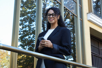 Portrait of young woman with phone wearing stylish suit outdoors