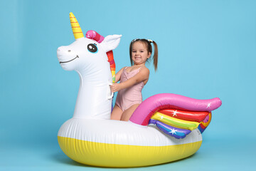 Cute little girl in swimsuit with unicorn pool float on light blue background © New Africa