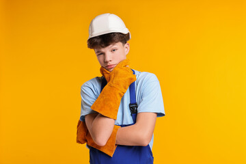 Teenage boy in hardhat working as builder on orange background