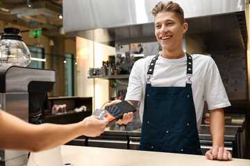 Cafe worker taking payment from client via terminal indoors