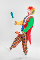 Funny clown juggling clubs on light background © New Africa