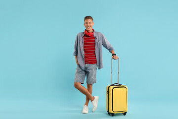 Happy traveller with suitcase on light blue background