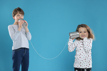 Boy and girl talking on tin can telephone against blue background