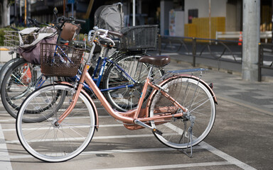 A bicycle parked in a bike bay on the streets on Japan during harsh sunlight in the city. Pink metallic paint with white wheels and other bikes in the background. Background no logos isolated focus