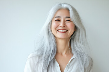 Fototapeta premium A beautiful smiling woman with long gray hair is wearing an elegant blouse and standing in front of the camera, with her head slightly tilted to one side as she smiles gently at something offscreen.