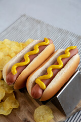 Homemade Boiled Hot Dogs with Mustard and Potato Chips on a Wooden Board, side view. Copy space.