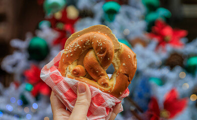Woman holds a foie gras pretzel sandwiches at the Chrismas Market in Strasbourg, France with a Christmas tree in the background