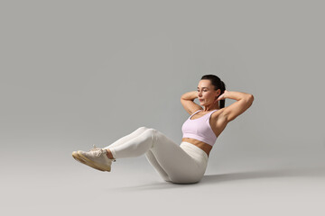 Woman in gym clothes doing abs exercise on grey background