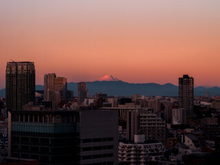 Central image of Mount Fuji peak and silhouette of mountains in the horizon with Tokyo city skyline in the foreground and deep red dawn sky. Land of the rising sun.