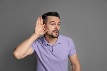 Man showing hand to ear gesture on grey background