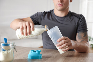 Making protein cocktail. Man pouring milk into shaker at wooden table, closeup