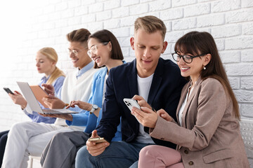 Group of people using different gadgets near white brick wall indoors. Modern technology