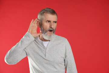 Senior man showing hand to ear gesture on red background. Space for text