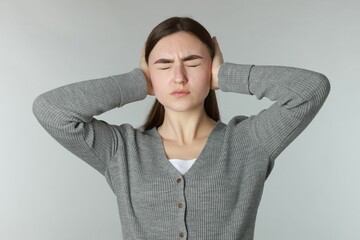 Distressed woman covering her ears from loud noise on light grey background