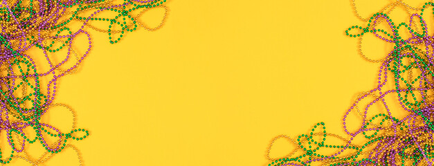Mardi Gras composition background. Festive yellow banner with colorful beads for Mardi Gras celebration. Top view flat lay. © prime1001